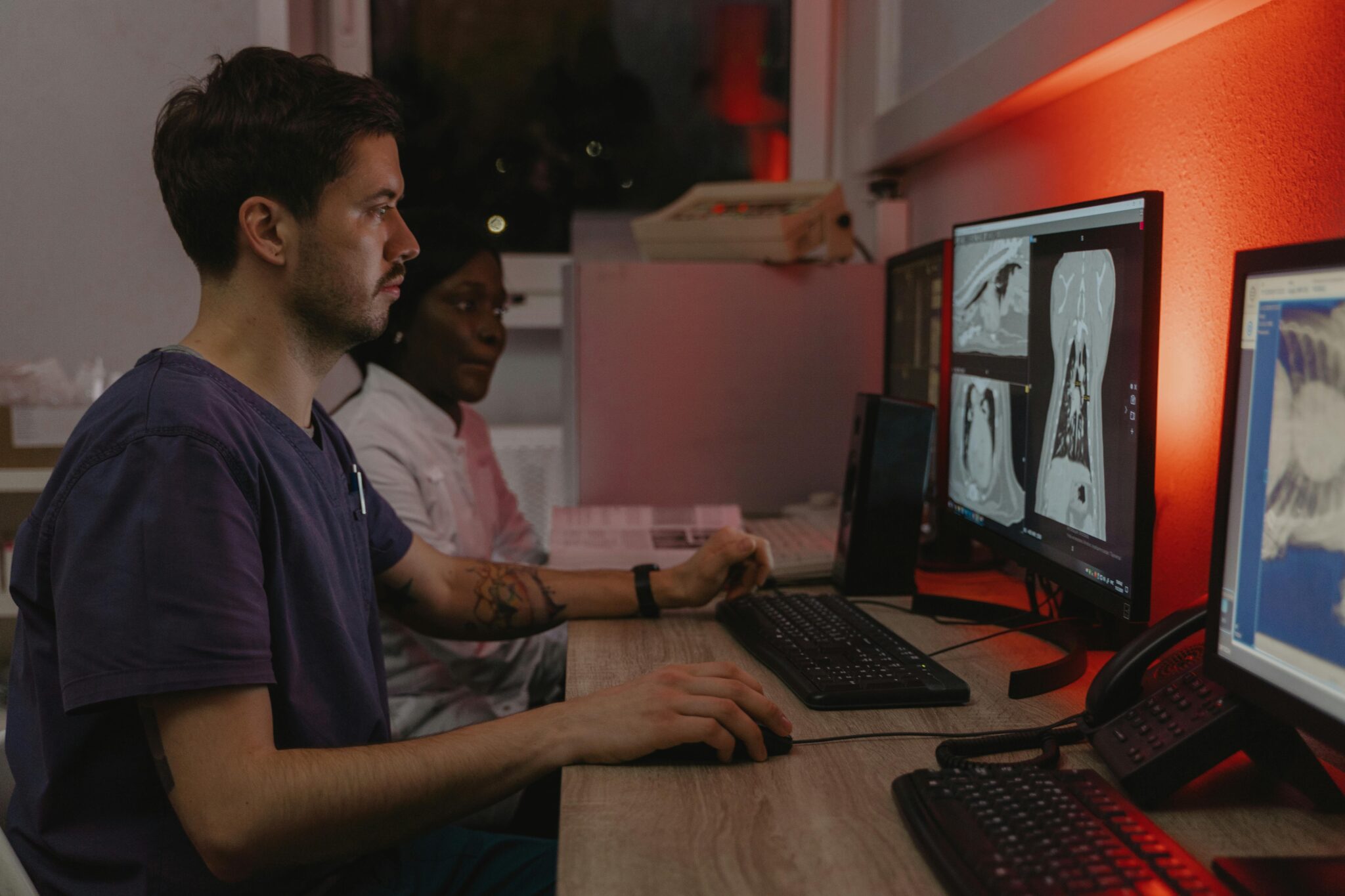 Two healthcare professionals working at computers analyzing medical scans in a clinical setting.